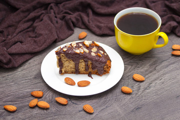 Slice of homemade banana bread with chocolate, almond and yellow cup of coffee on wooden background.