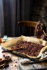 homemade baked chocolate granola with nuts, oat flakes on baking tray with parchment stands on grey wooden table