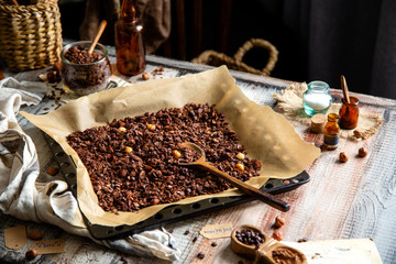 homemade baked chocolate granola with nuts, oat flakes on baking tray with parchment stands on grey wooden table