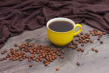 Yellow coffee cup and coffee beans on wooden background.