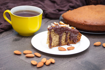 Slice of homemade banana bread with chocolate, almond and yellow cup of tea or coffee on wooden background.