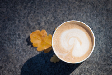 Paper blue coffee cup on the autumn fall leaves and stone grey background.