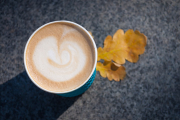 Paper blue coffee cup on the autumn fall leaves and stone grey background, copy spase
