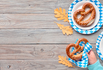 Oktoberfest, female hand holding pretzel, copy-space on wooden table