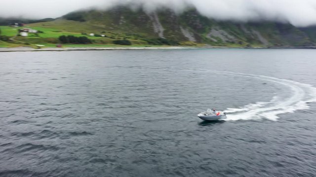 A motorboat speeds through the water near a rugged coastline and farms on the nearby shore