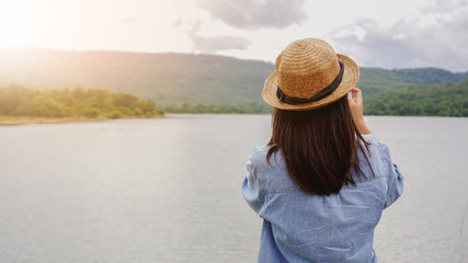 back of young woman in hat on the beach using smartphone camera capture the view.