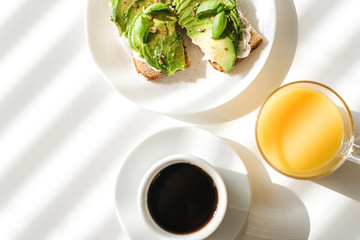 Avocado toasts and a cup of black coffee on a white table.