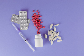 Packing pills and medical syringe. A scattering of tablets. Pills spilling out of a jar on a purple background.