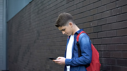 Schoolboy using cell phone in backyard, addiction to mobile games, social media