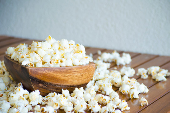 Salted popcorn on a wooden table. White popcorn flakes in a wooden bowl. Selective focus image.