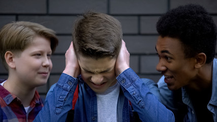 Depressed boy covering ears from mockery and insults of schoolmates, bullying