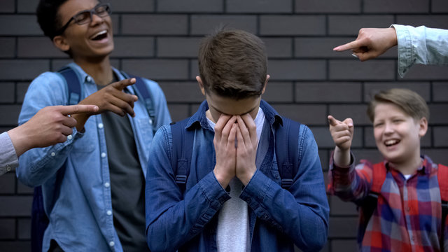 Cruel teenagers pointing at boy crying, emotionally depressed victim of bullying