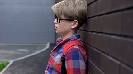 Upset schoolboy standing near wall, statistics of bullied children, awareness
