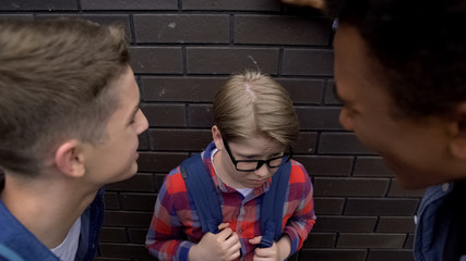Tall students bullying junior boy, teasing about small stature, domination