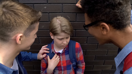 Impudent teenagers bullying weak boy, teasing about poor eyesight, small stature