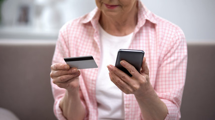 Senior female entering credit card number on smartphone, paying bills online