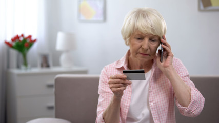 Confused aged woman with credit card calling bank support, payment problems