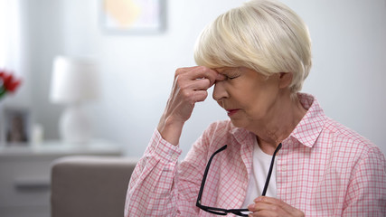 Aged woman taking off eyeglasses and massaging painful nose, migraine pain