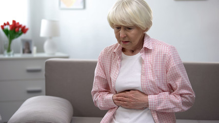 Upset old woman holding hands on stomach, suffering from gastritis disease