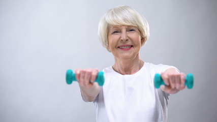 Senior woman with dumbbells smiling at camera, wellness, healthy lifestyle