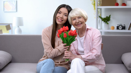 Old woman with granddaughter holding bunch of tulips and looking at camera