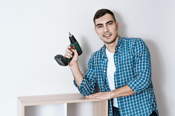 Portrait of a young beautiful European man with an electric screwdriver in his hand, a collector of furniture. copy space