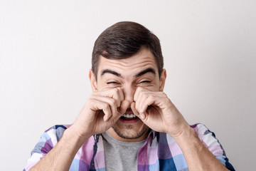 Close-up portrait of a young Caucasian man, rubs his eyes with his hands from tears of laughter, grief, pain.