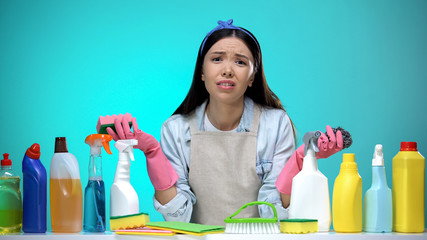 Confused housewife in gloves holding sponge, washing detergent hard choice