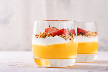 frontal two glasses with dessert Panna cotta from mango smoothie, ricotta, mussels and strawberry...