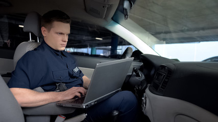Policeman working on laptop in patrol car, monitoring incident map, technology