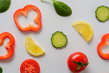 Flat lay design with sliced cucumber, tomato, lemon, bell pepper and spinach leaves with white background