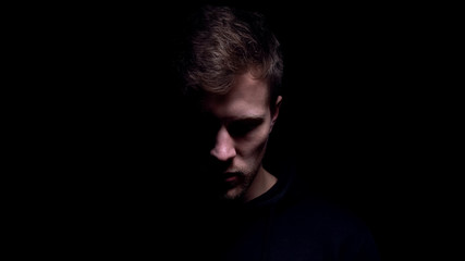 Man looking down against black background, feeling guilty for committed crime