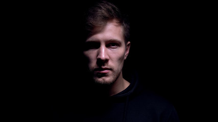Fototapeta premium Poważny młody człowiek patrząc na kamery, tajemnicza ciemność, straszny maniak
