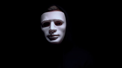 Man in terrible face mask staring at camera against dark background, terrorism