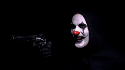 Contract killer in clown face mask aiming gun, crazy robber intimidating victim