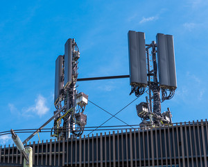 A mobile phone tower on a roof with a multiple wires and connections against a blue sky