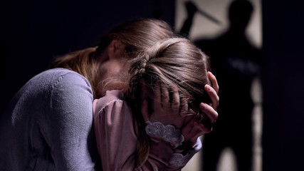 Daughter and mother watching crazy maniac with knife shadow outside door, fear
