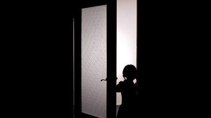 Little female child silhouette opening door into darkness, horror scene, mystic