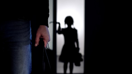 Silhouette of little girl entering room, violent father with belt on foreground