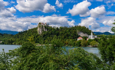 Fototapeta na wymiar View of Bled Castle and St. Martin's Church in the foreground green trees, beautiful clouds.