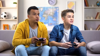 Excited multiethnic teen friends enjoying video games, free time at home © motortion