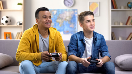 Smiling international teenager boys with joysticks playing video game, addiction