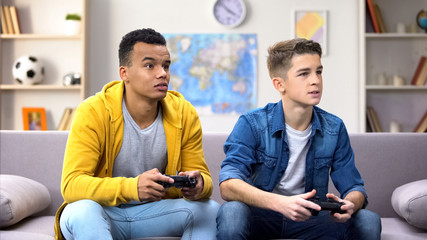 Afro-American and Caucasian teenager friends emotionally playing video game