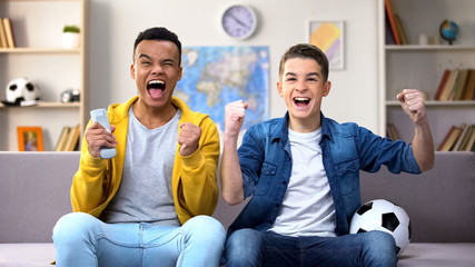 Multiracial teen boys rejoicing football team victory, watching match at home