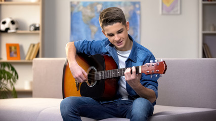 Cheerful Caucasian teenager playing guitar, enjoying favorite hobby, leisure