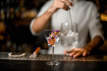 Bartender stirring a cocktail with a spoon in the focus foreground of flower decorated glass