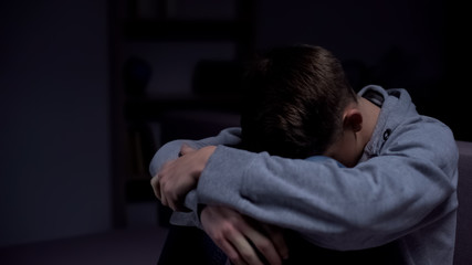 Depressed teenage boy sitting in dark room, misunderstanding with parents