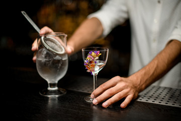 Professional bartender holding a cocktail measuring cup with a strainer and flower decorated glass