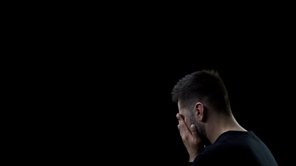 Fototapeta na wymiar Depressed man covering face by hands on dark background, mistake regret, problem