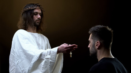 Savior in crown of thorns giving wooden cross necklace to praying man, hope
